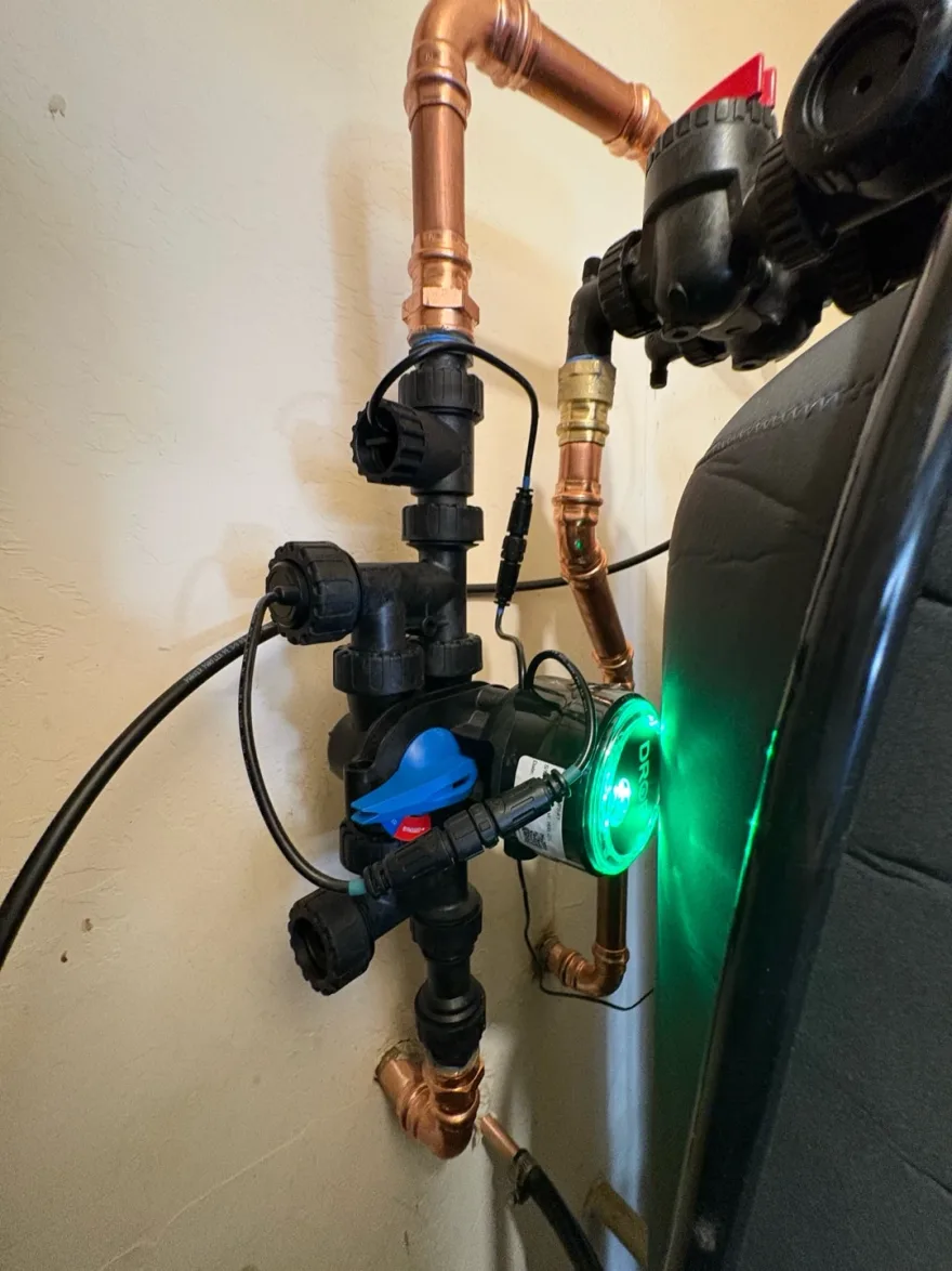 DROP leak detection unit with a glowing green status ring, plumbed into copper lines beside a water treatment tank