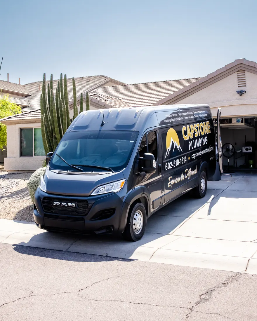 Capstone Plumbing's charcoal and gold service van parked in the driveway of a desert home beside a tall cactus