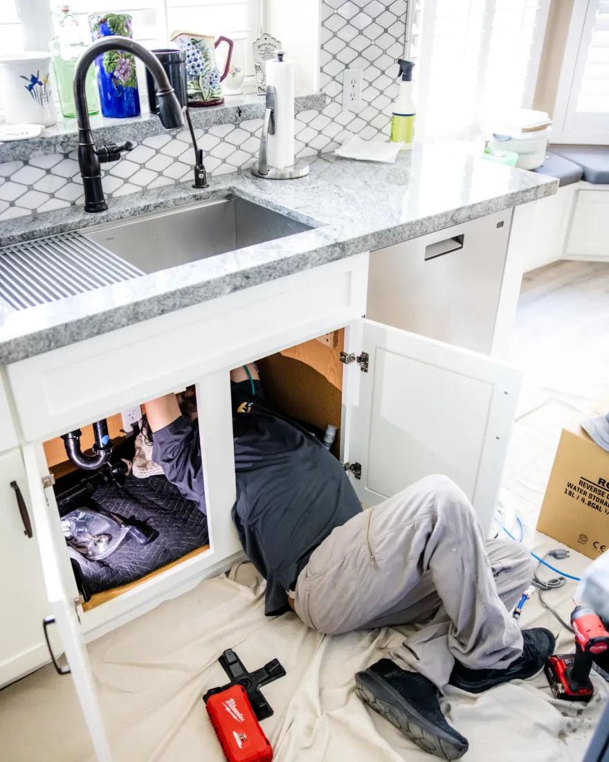 A Capstone plumber working under a kitchen sink with a drop cloth spread across the floor to protect it
