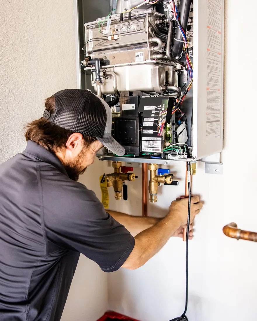 Capstone Plumbing technician servicing a tankless water heater with the cover off and the heat exchanger visible