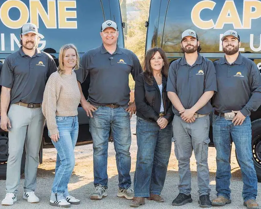The Capstone Plumbing team standing in front of their gold-and-black branded vans in Cave Creek, Arizona