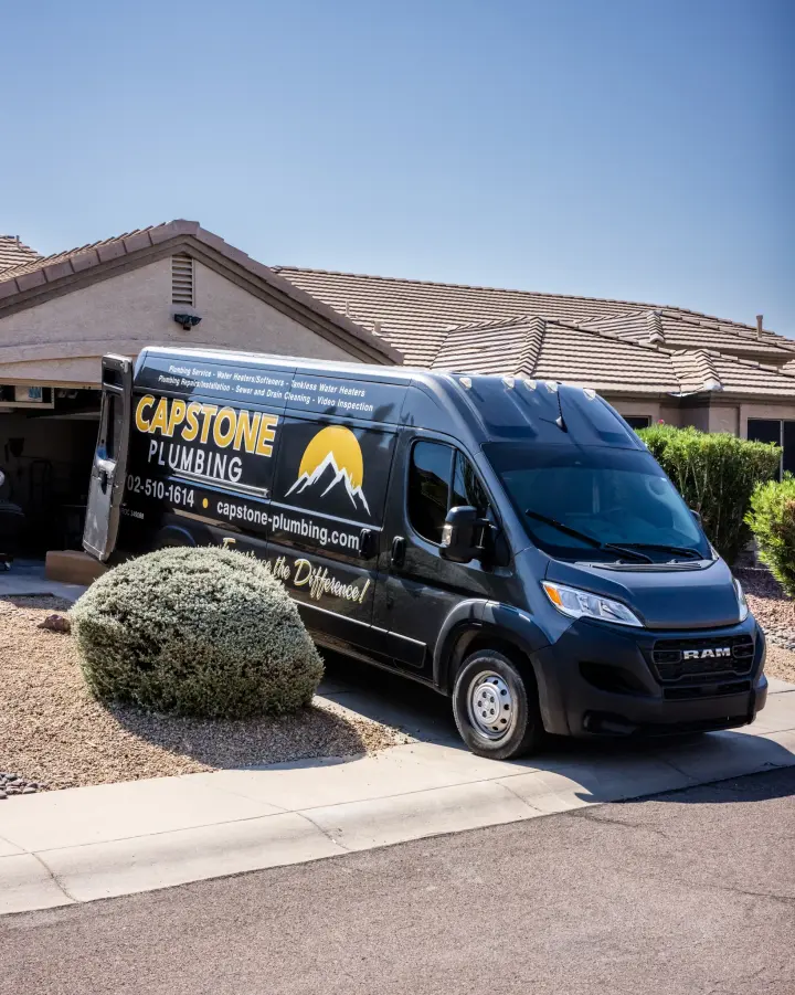 Capstone Plumbing service van parked in the driveway of a desert home, with the gold mountain logo, phone number, and services lettered on the side