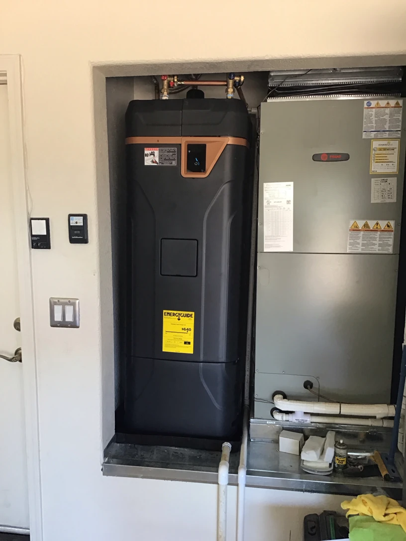 Tank water heater with a digital control panel installed in a garage alcove beside an air handler
