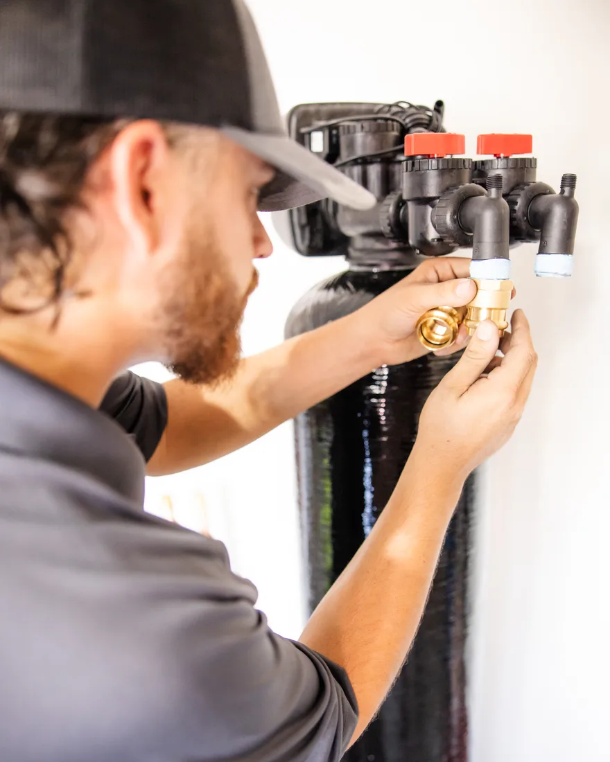 Capstone Plumbing technician attaching brass fittings to the control head of a whole-home water treatment tank